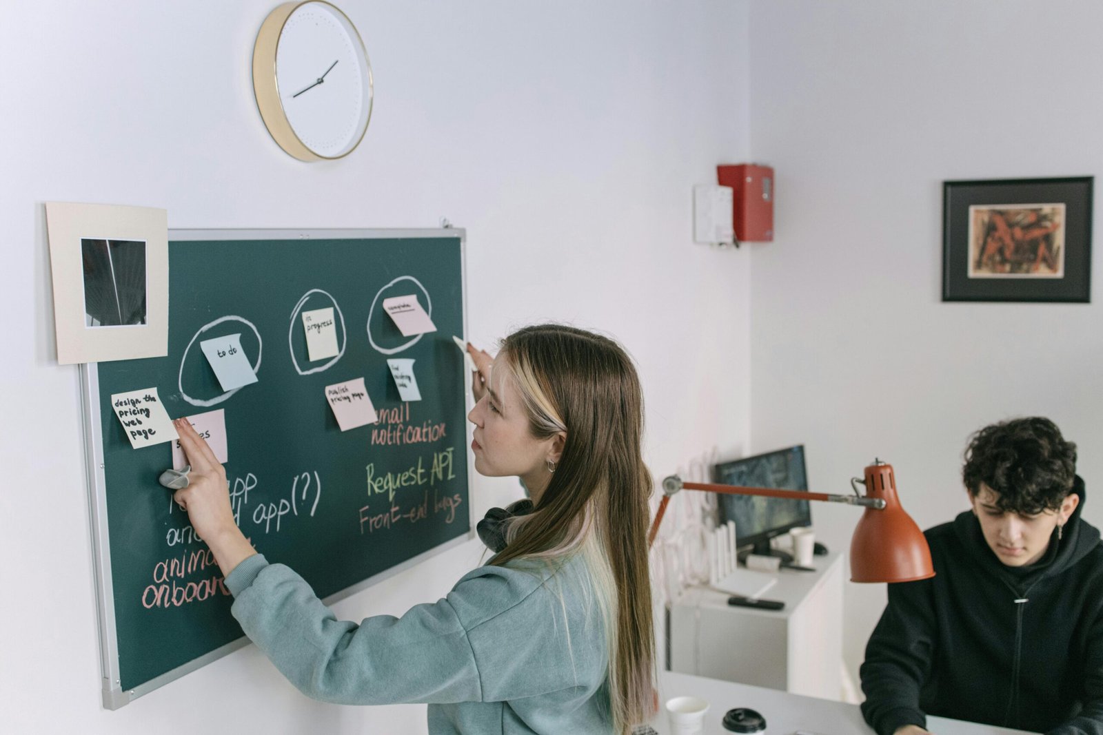 Two young coworkers brainstorming using sticky notes on a blackboard in a contemporary office setting.